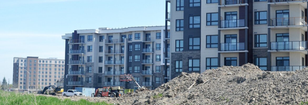 Construction site of modern apartment buildings with piles of dirt and construction equipment under a clear blue sky.