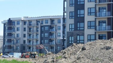 Construction site of modern apartment buildings with piles of dirt and construction equipment under a clear blue sky.