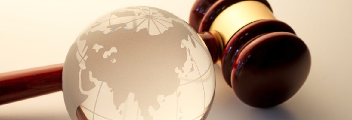 A wooden judge's gavel beside a transparent globe etched with a world map, symbolizing international law and justice.