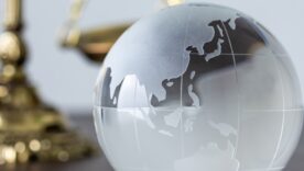 A globe-inspired glass paperweight on a desk with a portion of the scales of justice visible in the background
