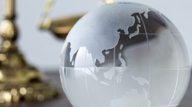 A globe-inspired glass paperweight on a desk with a portion of the scales of justice visible in the background