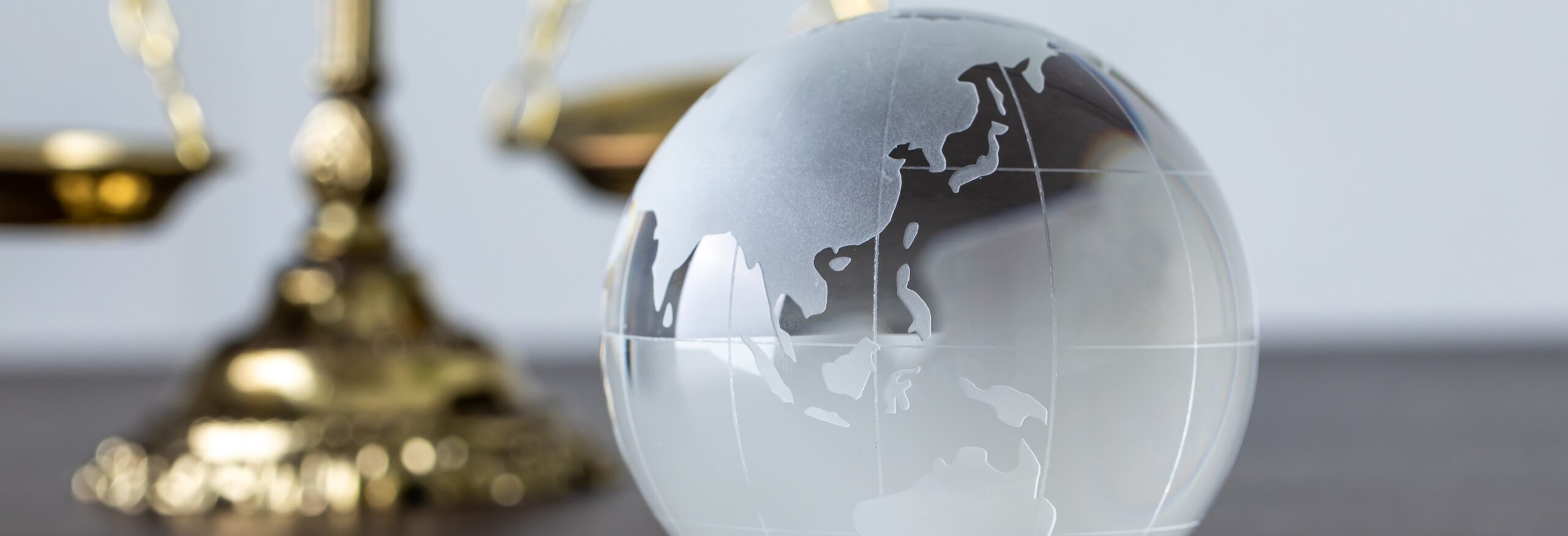 A globe-inspired glass paperweight on a desk with a portion of the scales of justice visible in the background
