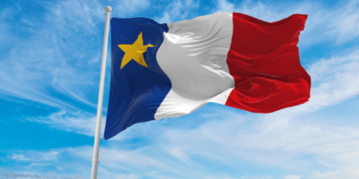 Flag of the French region Occitanie with blue, white, and red vertical stripes and a yellow star in the blue section, waving against a blue sky.