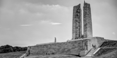 Black and white photo of a large stone war memorial with tall pillars and statues on a grassy hill with visitors walking around.