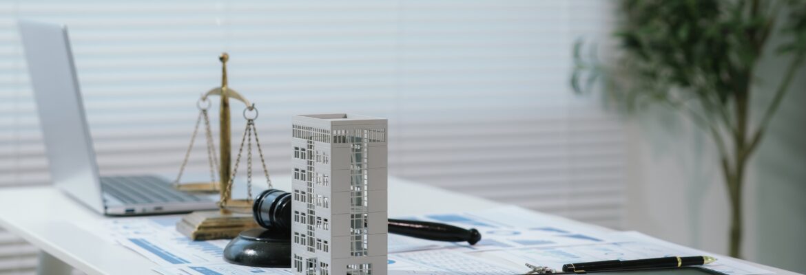 Justice scale and judge gavel beside building model and business reports, representing real estate law, fair property transactions, and housing regulations