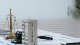 Justice scale and judge gavel beside building model and business reports, representing real estate law, fair property transactions, and housing regulations