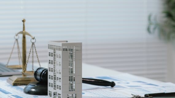 Justice scale and judge gavel beside building model and business reports, representing real estate law, fair property transactions, and housing regulations